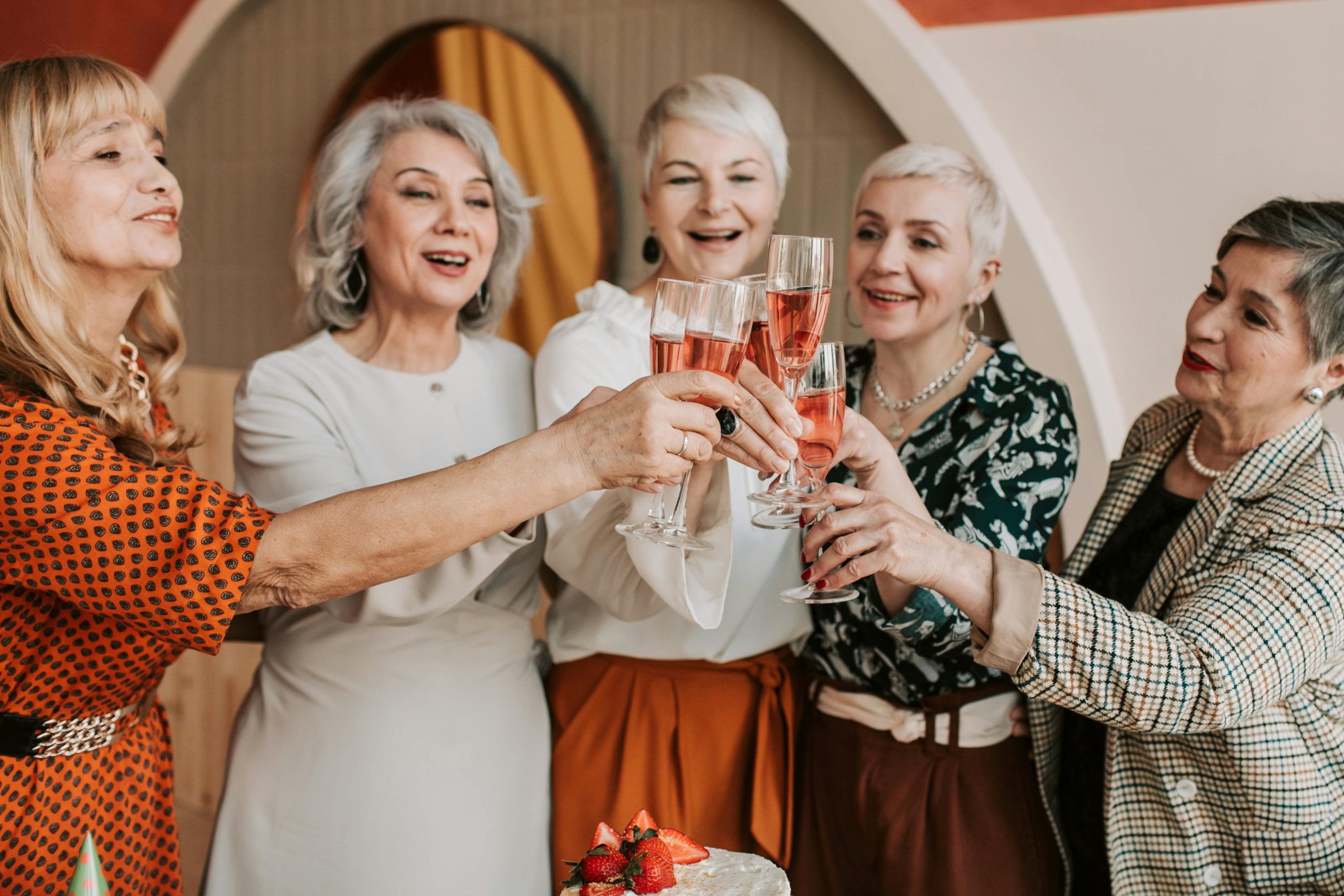 A group of senior women celebrating with a toast of champagne indoors, radiating happiness and togetherness.